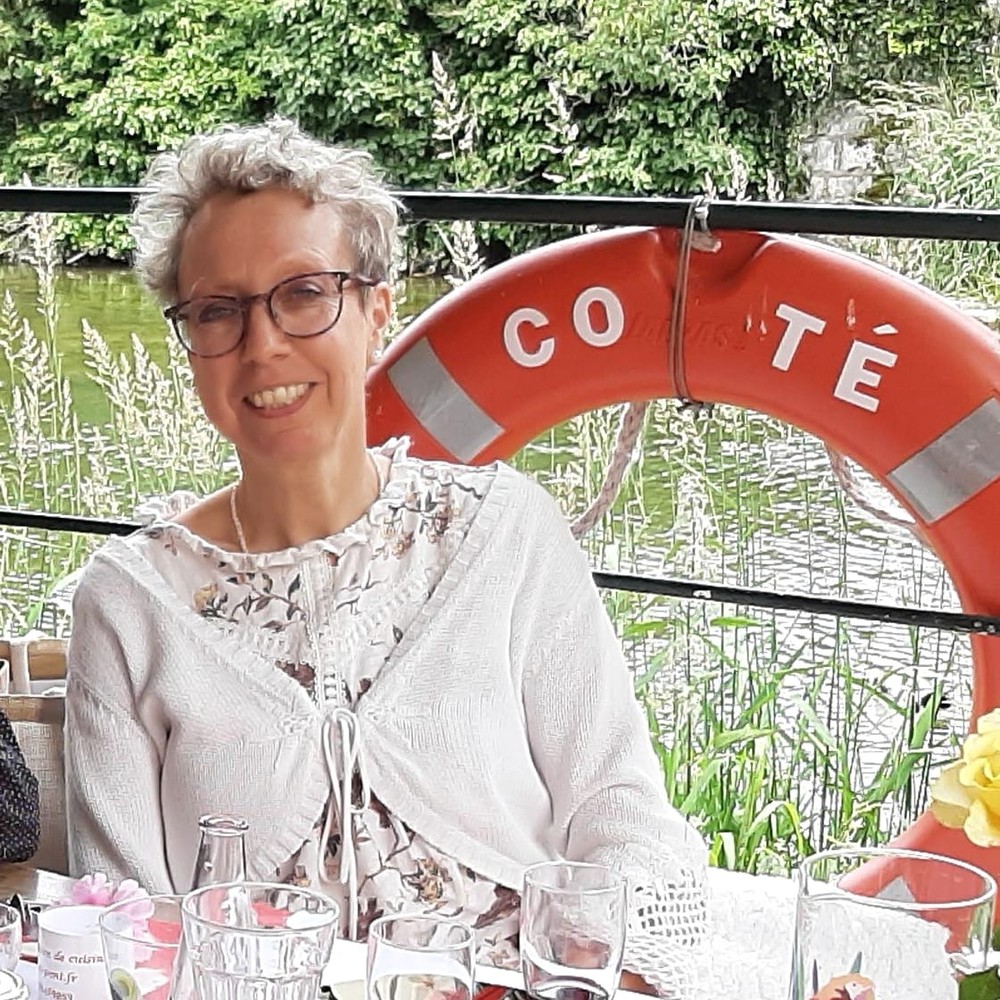 Emmanuelle Girard Mukuna, souriante, attablee au bord de l’eau.